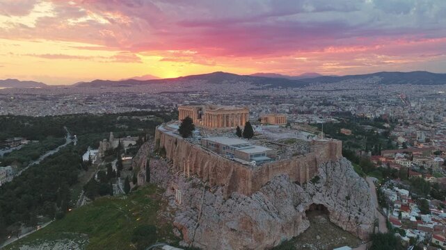 Aerial view of the famous acropolis of athens and the parthenon temple with a dramatic and colorful sunset sky, showing the ancient citadel overlooking the sprawling cityscape of greece's capital