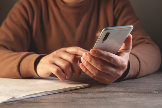 Close-up of a male hand holding a mobile phone and taking notes.