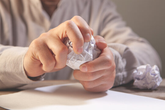 Man hand crumpling a paper with crumpled paper ball