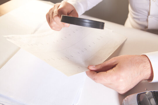 Close up of male hands holding a magnifying glass and a document