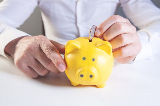 Businessman putting coin into a piggy bank, close-up