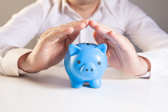 Businessman holding blue piggy bank in hands. Saving money concept