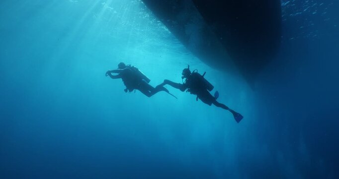scuba diver scenery under the parked boats with sun beams and rays underwater