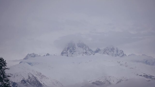 Ushba mountain peak partially hidden in clouds, Caucasus, Georgia. Zooming handheld shot of snowy summit in mist, cold moody alpine atmosphere