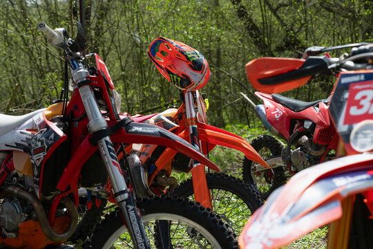Vladikavkaz, Russia - April 18 , 2026 :     Group of modern enduro motorcycles parked in a forest during a sunny day with a professional motocross helmet on handlebars
