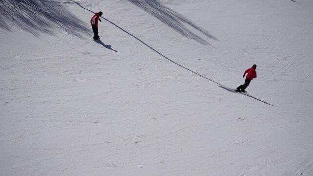 Slow motion snowboarders riding on groomed ski slope in sunny winter day, white snow, minimal landscape, alpine resort, outdoor sport and active lifestyle