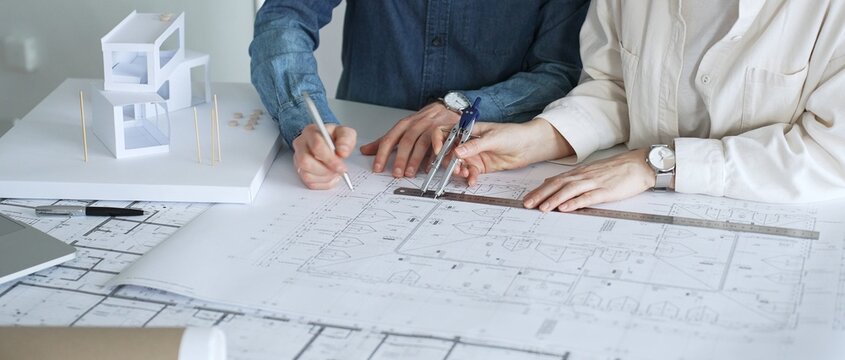 Architects working together, developing a building design by assembling a scale model and reviewing detailed blueprints, symbolizing teamwork, planning, and architectural creation