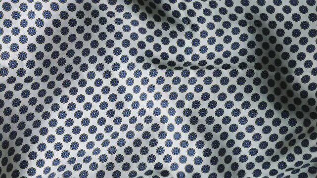 Moving silk fabric with a geometric floral pattern creates an abstract background of soft waves. The blue and black circular ornaments on the white surface ripple smoothly as the natural silk material
