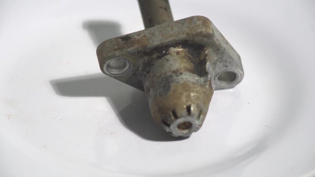 Detailed 4K shot of a used motorcycle cam chain tensioner rotating on a white surface. Highlighting mechanical engine components, maintenance needs, and automotive engineering parts for professional r