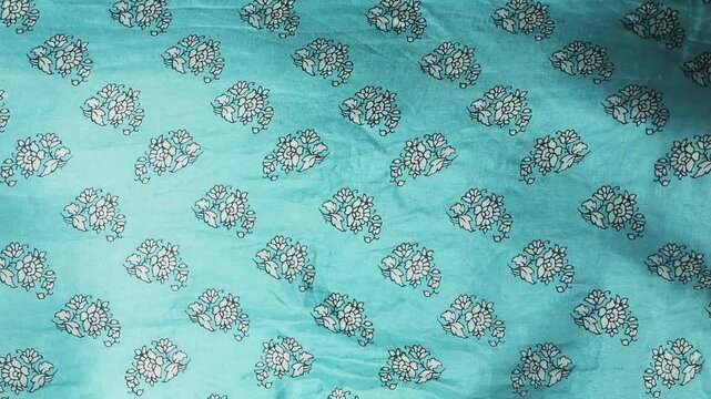 Natural silk fabric with floral pattern waving in the wind. Turquoise textile creating abstract background with soft waves. Detailed view of traditional block print design on flowing cloth. 