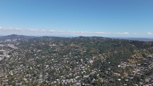 Aerial wide shot of Sherman Oaks neighborhood in Los Angeles during summer, showing dense residential homes across rolling hills under clear blue sky. Suburban sprawl and urban landscape in USA.