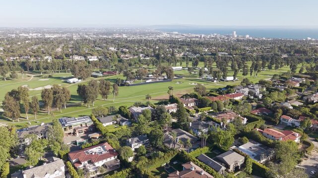 Aerial view of Riviera Country Club with luxury mansions in Pacific Palisades Los Angeles and Santa Monica skyline and ocean in background under clear sunny sky upscale coastal living. Wide shot.