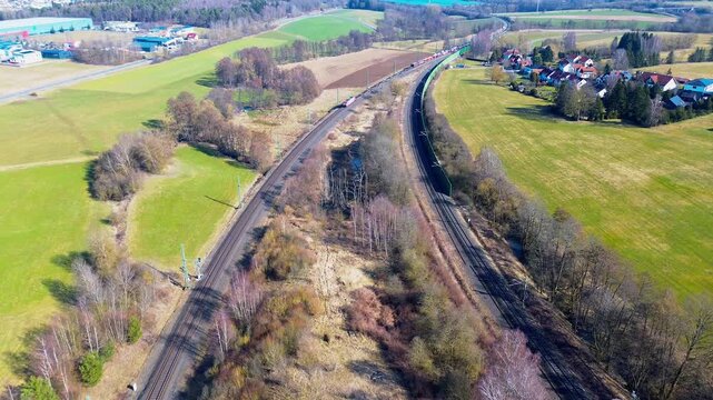 Aerial view of freight train on parallel railway tracks through rural farmland near village in Germany