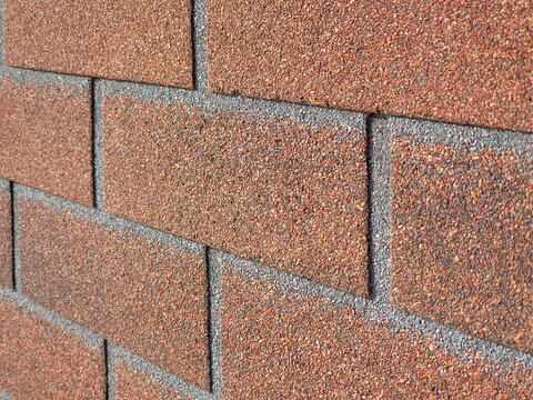 Facade tiles imitating red brick. Close-up, side view. Texture building material used for cladding basement of house. Tiles are sprinkled with stone chips, imitating brickwork.