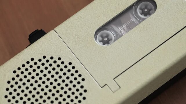 Angled close up of beige voice recorder with spinning tape reels and tape window