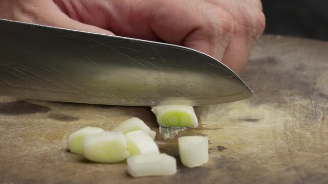 Slicing a fresh leek on a wooden board with a sharp knife