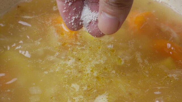 Hand adding salt to soup, enhancing flavor and taste, kitchen scene