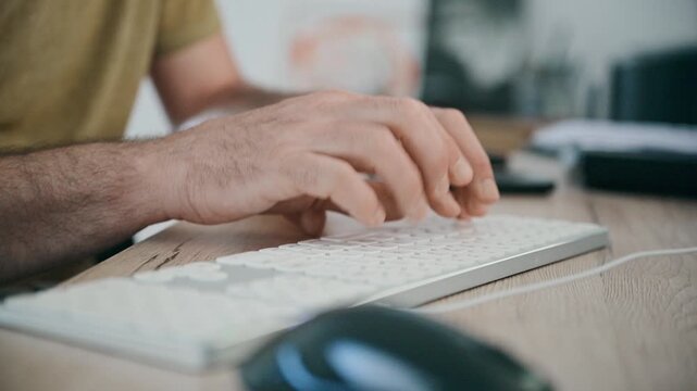 Male hands type on a slim computer keyboard at a wooden desk, with a mouse and monitor nearby conveying focused office work, typing, remote work and everyday productivity in a modern workspace. 4K