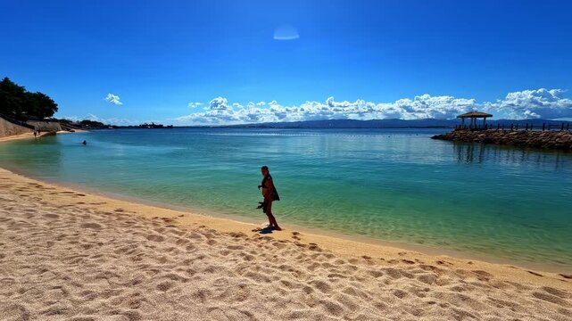 Woman walks by clear blue water on beach at Dusit Thani Mactan Cebu resort Philippines