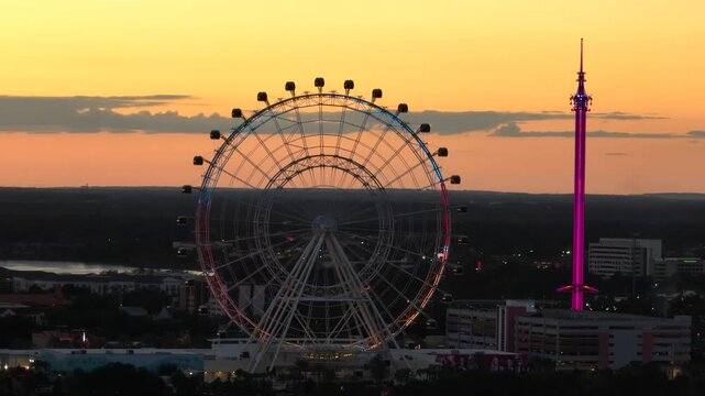 Cinematic nighttime aerial footage of the illuminated Orlando Eye Ferris wheel and ICON Park attractions against a vibrant sunset.