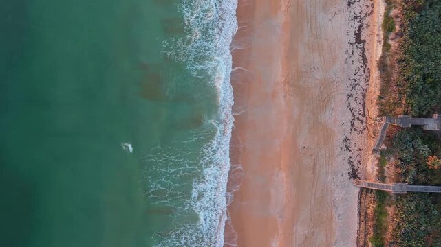 Cinematic birds-eye drone footage of ocean waves hitting the shore and wooden beach access boardwalks in Saint Augustine, Florida.