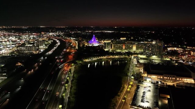 Cinematic nighttime aerial footage of the illuminated downtown Orlando skyline and heavy traffic flow on Interstate 4.