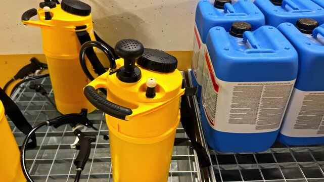 Yellow pump sprayers with blue plastic containers on a metal grid, storing liquids