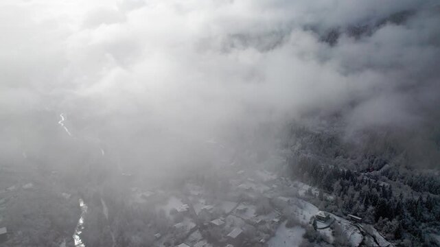 Drone descending through clouds over snowy mountain village and pine forest, Svaneti, Georgia. Winter landscape, Caucasus mountains, misty aerial view, cinematic nature scene