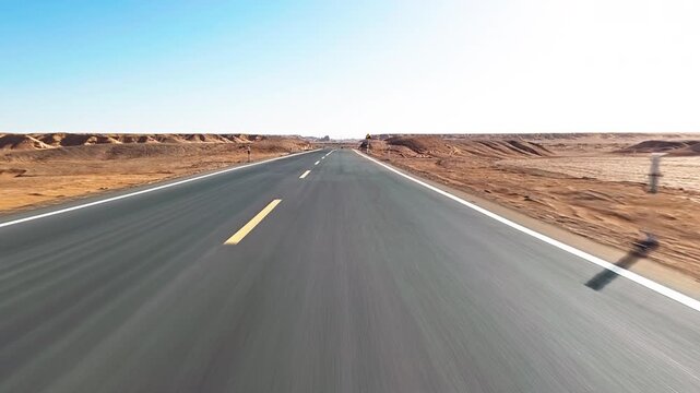 Empty asphalt road stretching through a vast arid desert landscape under a clear blue sky in Xinjiang, China