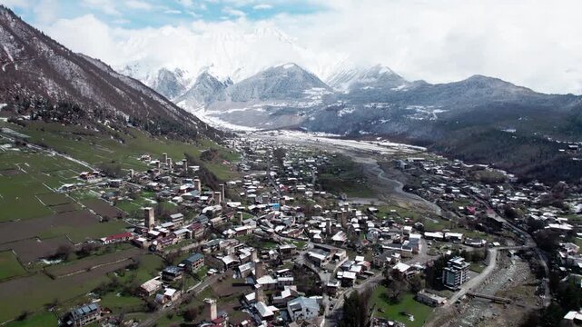 Aerial drone view of Mestia in Svaneti, Georgia with green valleys mixed with snow and high mountain peaks. Scenic landscape with traditional architecture, nature, travel, winter transition