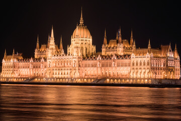 Obraz premium Stunning night view of the illuminated Hungarian Parliament Building reflecting on the Danube River in Budapest.