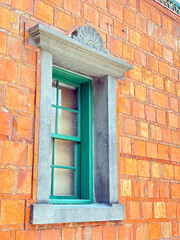Fototapeta premium A vibrant close-up of a vintage teal wooden window set against a weathered orange brick wall. The high-contrast color palette and architectural framing highlight traditional textures and rustic charm.