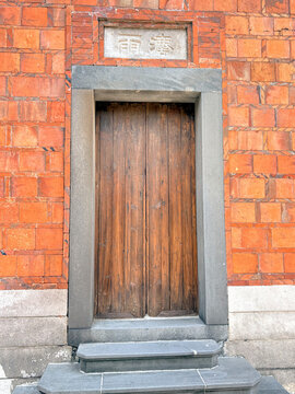 Frontal view of an ancient wooden door framed by a heavy stone lintel and red brick walls. A classic example of traditional vernacular architecture.