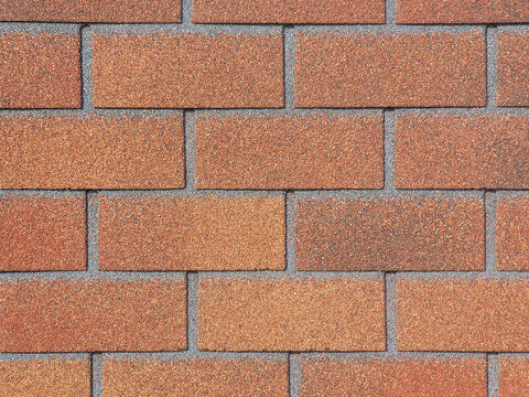Facade tiles imitating red brick. Close-up. Texture building material used for cladding basement of house. Tiles are sprinkled with stone chips, imitating brickwork.