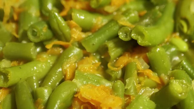 Fresh green beans and bright shredded carrots simmer together in a savory sauce inside a hot pan. Concept of healthy eating, vegetarian meal preparation, and wholesome home cooking.
