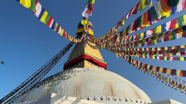 Slow motion pigeons flying around Boudhanath stupa in Kathmandu with colorful prayer flags waving in the wind. Spiritual atmosphere, Buddhism, travel, peaceful scene, cultural landmark