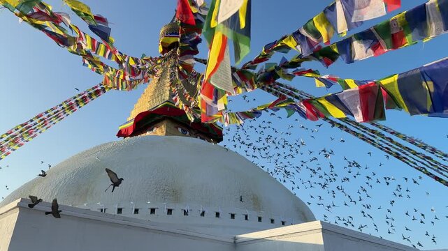 Slow motion pigeons flying around Boudhanath stupa in Kathmandu with colorful prayer flags waving in the wind. Spiritual atmosphere, Buddhism, travel, peaceful scene, cultural landmark
