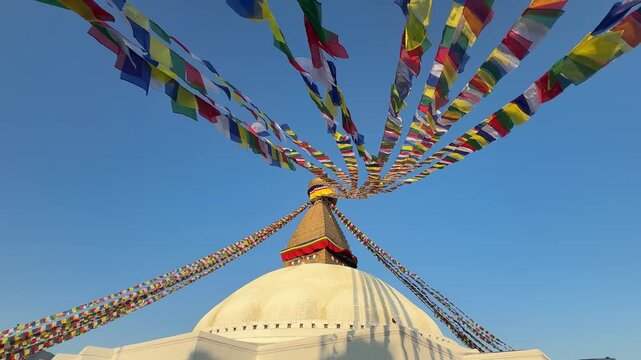 Slow motion prayer flags waving over Boudhanath Stupa in Kathmandu, Nepal. Spiritual Buddhist scene, calm zen atmosphere, blue sky, peaceful meditative background