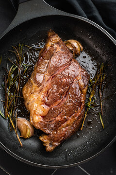 Seared beef chuck eye roll steak in skillet with rosemary and butter. Gourmet beef dish with rich flavor and copy space.