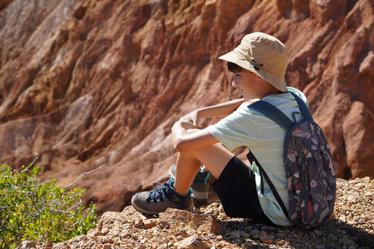 boy resting sitting on the rocks during a trkking on family vacation with reddish rocks in the background
