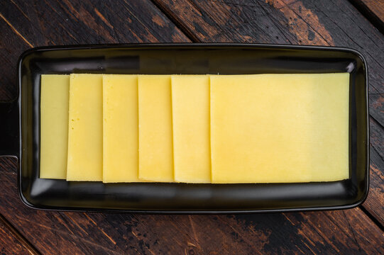 Stack of semi hard yellow cheese slices arranged on black tray, dairy ingredient on vintage wooden table background