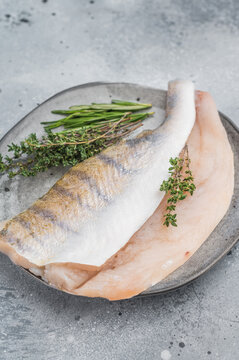 Raw pike perch fillets with skin and fresh herbs on light background, lean freshwater white fish for healthy cooking.