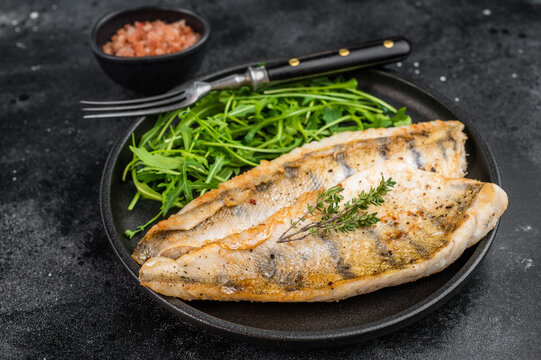 Pan fried pike perch fillet served with fresh arugula in plate, healthy freshwater fish meal.