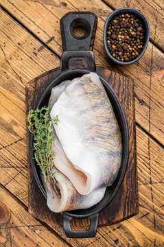 Raw pike perch fillets with skin in cast iron pan on rustic wooden table, fresh lean freshwater white fish with copy space.