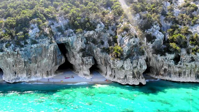 Cala Luna in Sardinia, Italy showcases stunning cliffs and turquoise waters perfect for a relaxing holiday. Visitors enjoy the serene beach, sunbathing, and swimming in a picturesque setting.