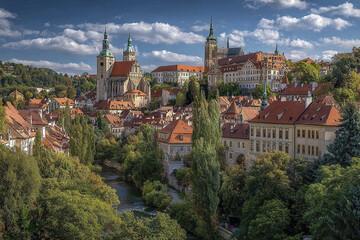 Obraz premium Panoramic skyline of European old town with church towers, red rooftops, and lush green trees under partly cloudy sky creating peaceful and historic atmosphere