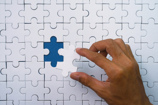 Human hand carefully places the last white puzzle piece into place