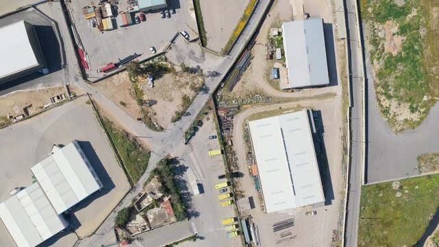 Zenithal aerial view showing a drone slowly flying over an industrial area with warehouses, factories, and commercial buildings, highlighting modern logistics and manufacturing infrastructure