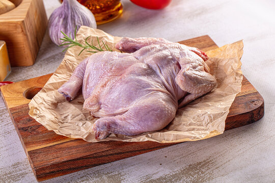 Raw whole chicken on a wooden cutting board with fresh herbs, spices, and vegetables.