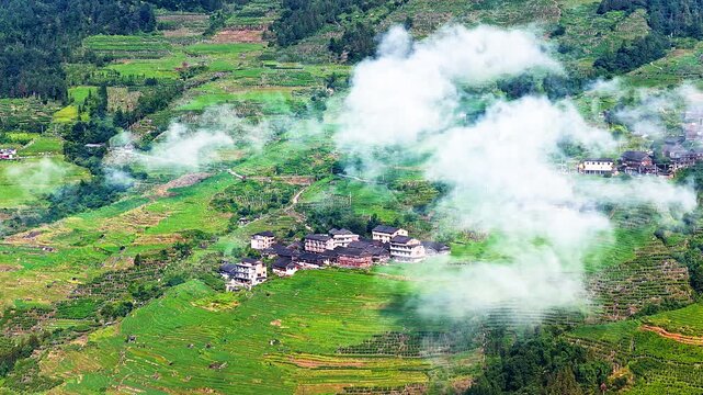 Aerial view of traditional rural village built on green terraced hillsides under moving clouds in Guilin, China.